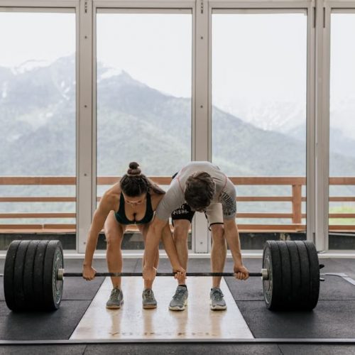 A couple lifting a heavy barbell together in a gym with mountain views.